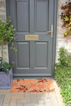 RHS Bloom Coir Collection Maple Leaves doormat in front of a grey door